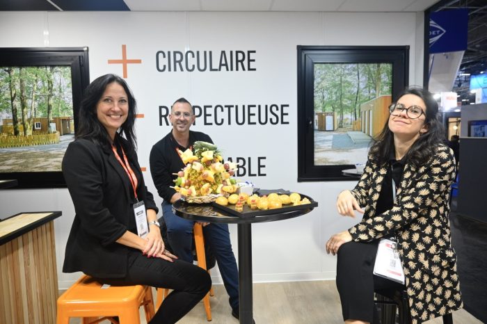 Photo of three people sitting around a small, round table with fruit and cheese on it.