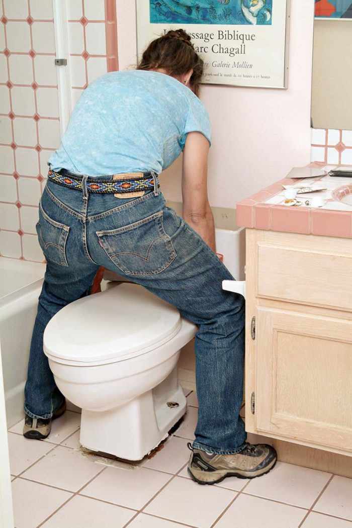 Straddle the toilet and lift straight up and off the sewer flange and bolts.